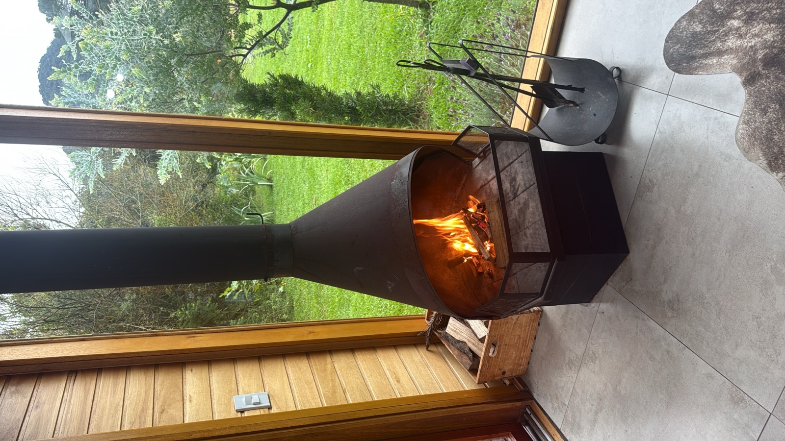 A fire pit glowing on a wooden deck over a green garden