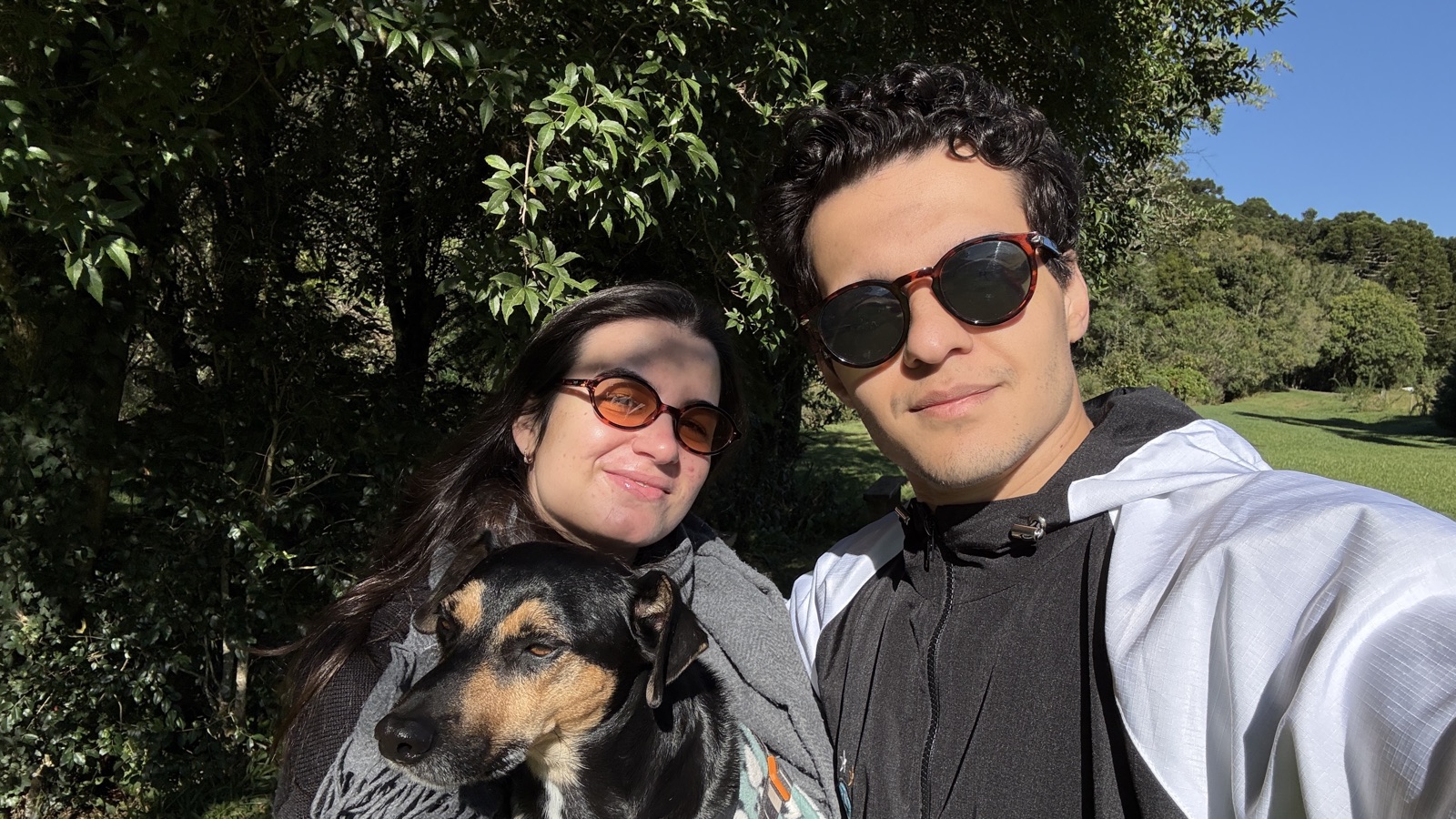 A couple and their dog smiling together on a sunny walk